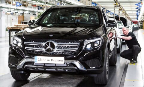 Ein Mann kniet neben einem neu produzierten dunklen Mercedes.